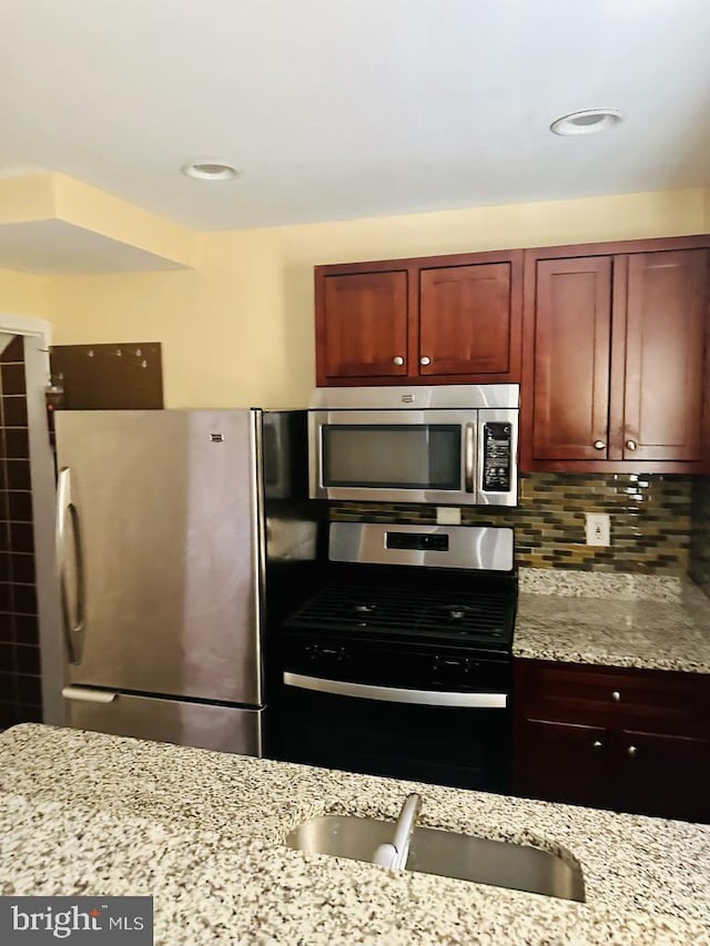 kitchen with light stone countertops, appliances with stainless steel finishes, backsplash, and sink