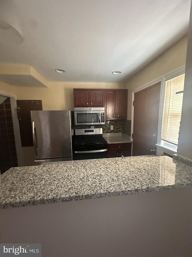 kitchen with light stone countertops, appliances with stainless steel finishes, and decorative backsplash