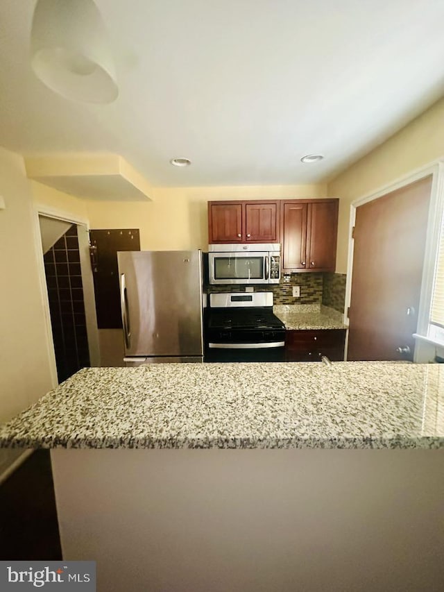 kitchen with backsplash, light stone countertops, and stainless steel appliances