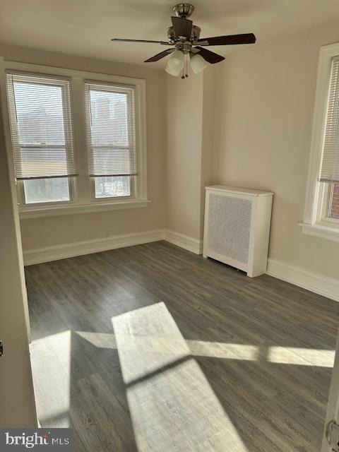 empty room featuring dark hardwood / wood-style floors, radiator, and ceiling fan