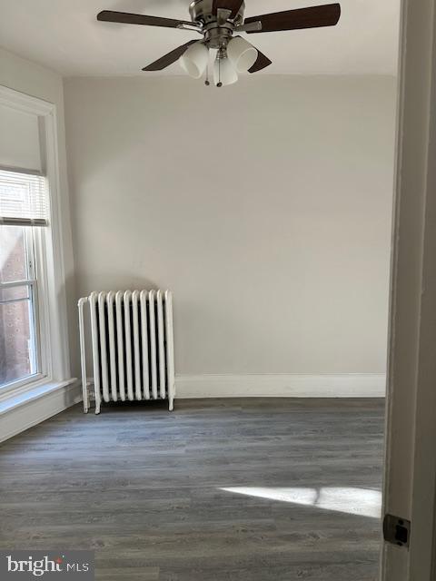 empty room with ceiling fan, radiator heating unit, and dark hardwood / wood-style floors