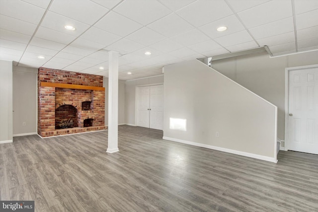 unfurnished living room featuring a paneled ceiling, hardwood / wood-style floors, and a brick fireplace