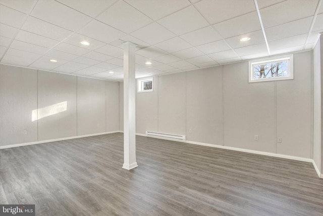 basement featuring baseboard heating, a healthy amount of sunlight, and dark hardwood / wood-style floors