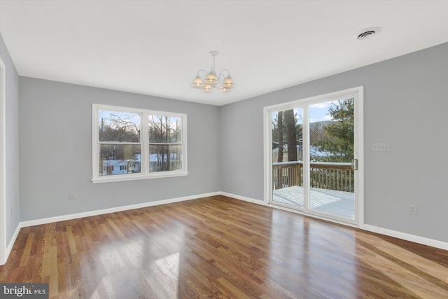 unfurnished room featuring a healthy amount of sunlight, wood-type flooring, and an inviting chandelier