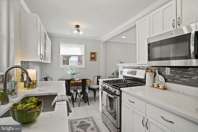 kitchen with white cabinetry, decorative backsplash, light stone counters, stainless steel appliances, and crown molding