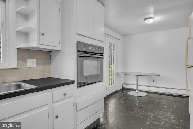 kitchen featuring backsplash, sink, oven, a baseboard radiator, and white cabinetry