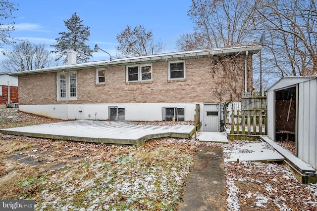 snow covered rear of property featuring a deck and a storage shed