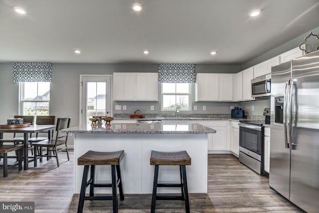 kitchen with light stone countertops, a center island, stainless steel appliances, dark hardwood / wood-style flooring, and white cabinets