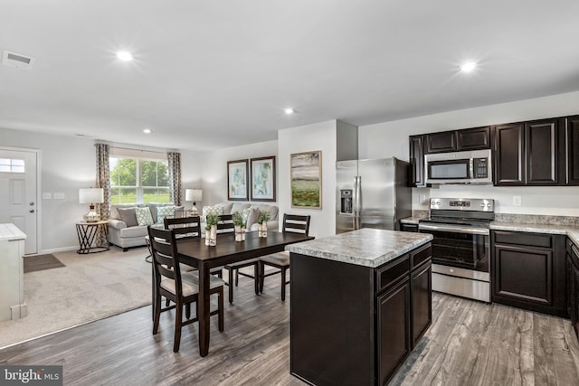 kitchen with appliances with stainless steel finishes, light hardwood / wood-style flooring, dark brown cabinets, and a center island