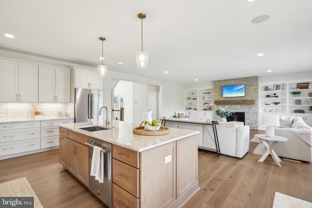 kitchen featuring stainless steel appliances, white cabinets, decorative light fixtures, a center island with sink, and a stone fireplace