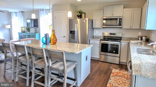 kitchen with a center island, sink, appliances with stainless steel finishes, decorative light fixtures, and a breakfast bar area