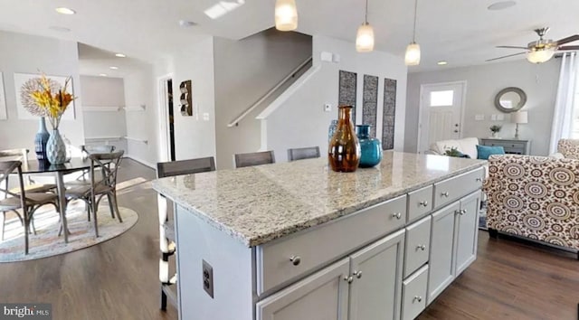 kitchen with light stone countertops, dark hardwood / wood-style flooring, ceiling fan, decorative light fixtures, and a center island