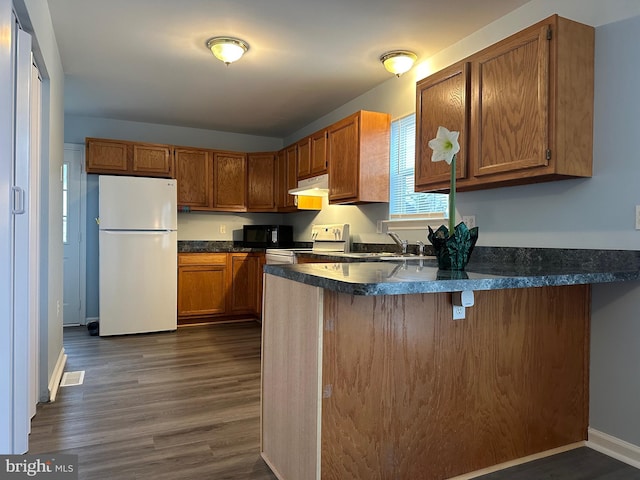 kitchen with sink, white appliances, a kitchen breakfast bar, dark hardwood / wood-style floors, and kitchen peninsula