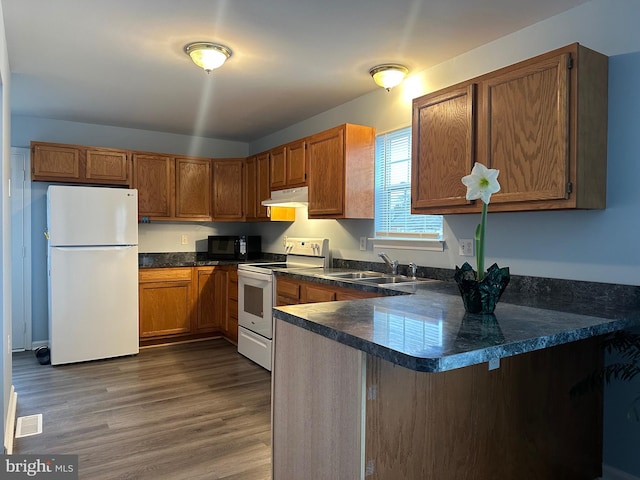 kitchen with dark hardwood / wood-style flooring, sink, white appliances, and kitchen peninsula