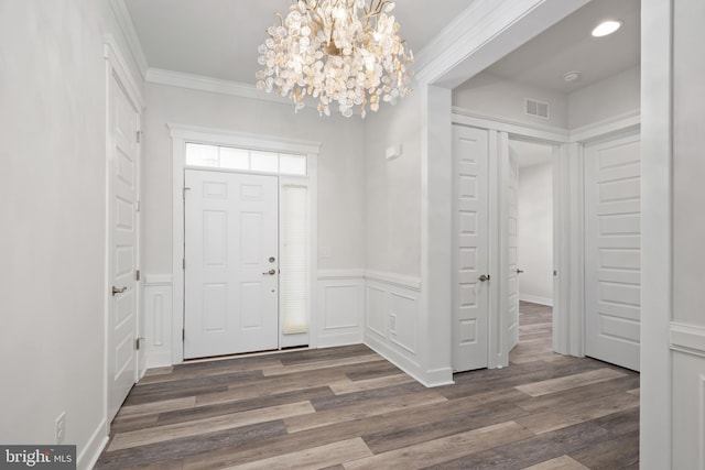 foyer with dark hardwood / wood-style flooring, crown molding, and an inviting chandelier