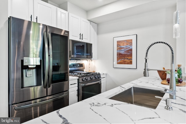 kitchen with pendant lighting, white cabinets, sink, light stone countertops, and appliances with stainless steel finishes