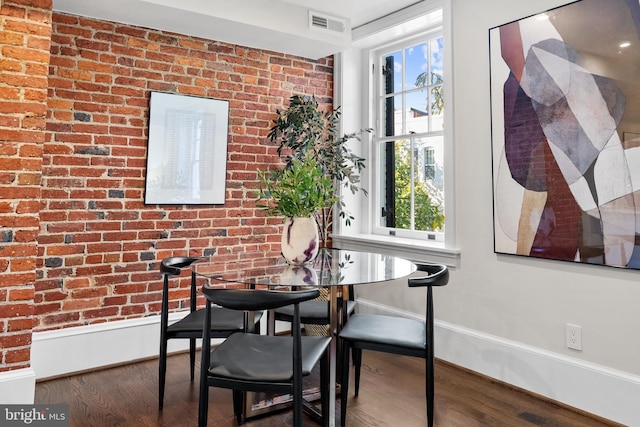 dining room with hardwood / wood-style flooring, a wealth of natural light, and brick wall