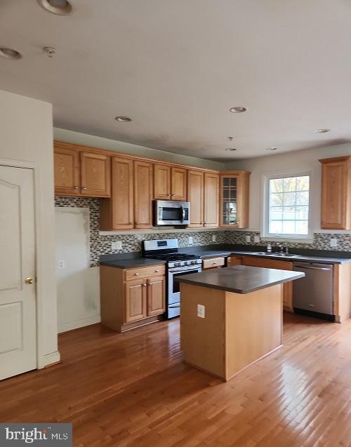 kitchen featuring decorative backsplash, light hardwood / wood-style flooring, a kitchen island, and appliances with stainless steel finishes