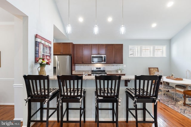 kitchen with pendant lighting, backsplash, stainless steel appliances, and a breakfast bar area