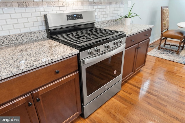 kitchen featuring light hardwood / wood-style flooring, light stone counters, backsplash, and stainless steel gas range