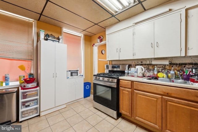 kitchen featuring light tile patterned flooring, a paneled ceiling, refrigerator, sink, and stainless steel gas range oven