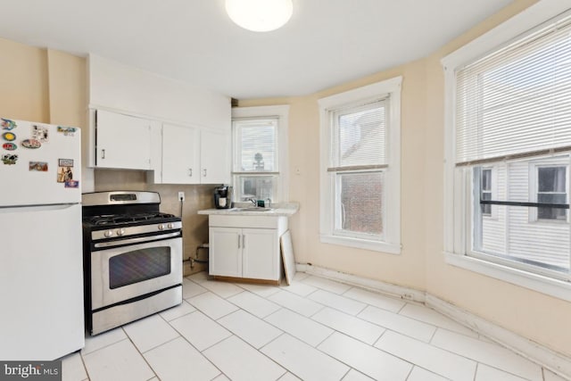 kitchen featuring white refrigerator, white cabinetry, sink, and gas stove