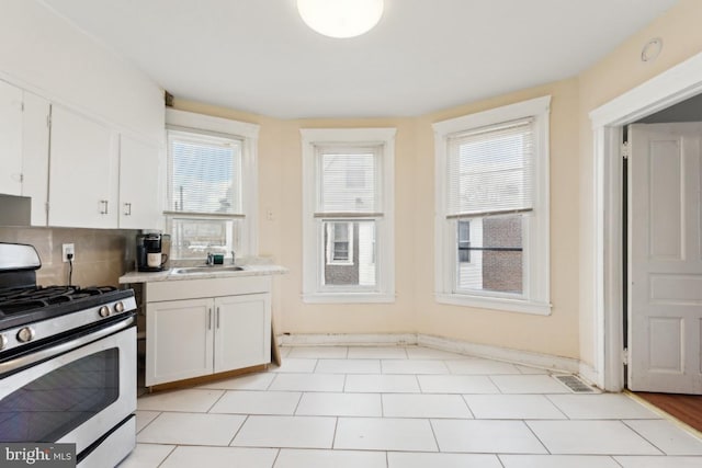 kitchen with gas range, sink, decorative backsplash, and white cabinets