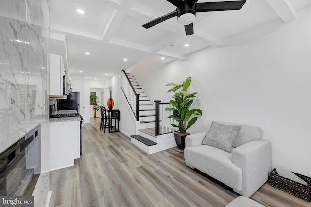 interior space featuring beam ceiling, ceiling fan, coffered ceiling, a premium fireplace, and light hardwood / wood-style floors