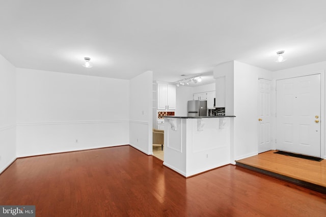 kitchen with stainless steel fridge, white cabinetry, dark hardwood / wood-style floors, and kitchen peninsula