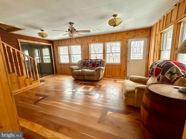 sitting room featuring a textured ceiling, light wood-type flooring, ceiling fan, and wooden walls