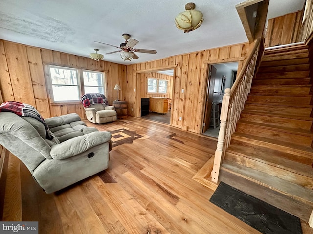 living room with a textured ceiling, hardwood / wood-style flooring, ceiling fan, and wood walls