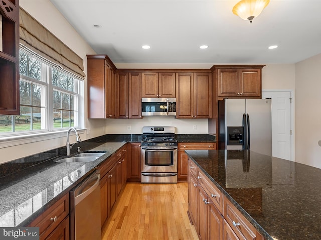 kitchen featuring dark stone counters, sink, appliances with stainless steel finishes, and light hardwood / wood-style flooring