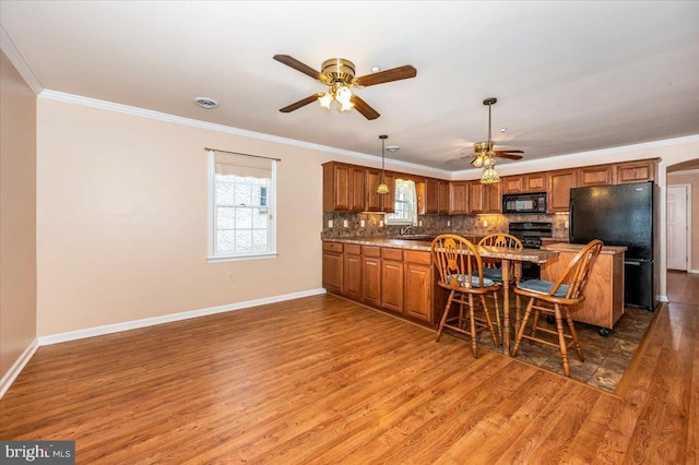 kitchen featuring black appliances, ornamental molding, tasteful backsplash, dark hardwood / wood-style flooring, and a breakfast bar area