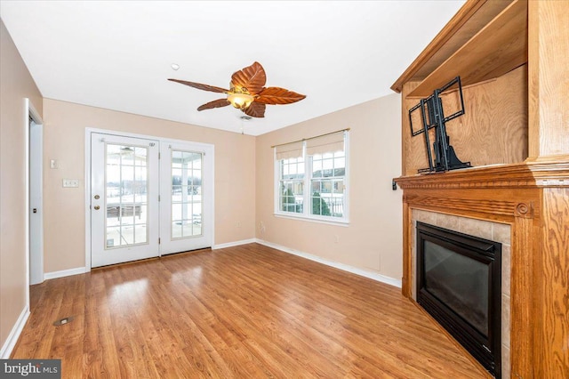 unfurnished living room featuring plenty of natural light, ceiling fan, light wood-type flooring, and a tiled fireplace