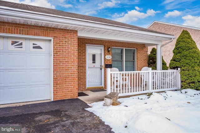 snow covered property entrance with a porch and a garage