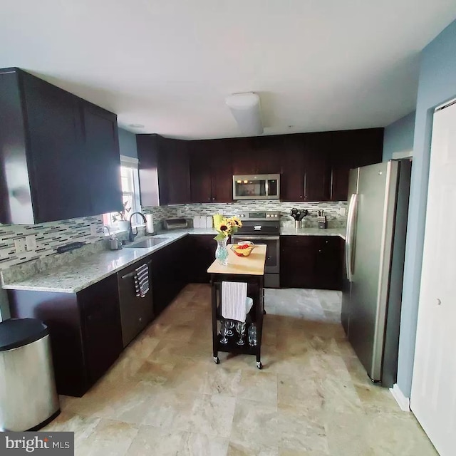 kitchen with sink, stainless steel appliances, tasteful backsplash, light stone counters, and dark brown cabinets