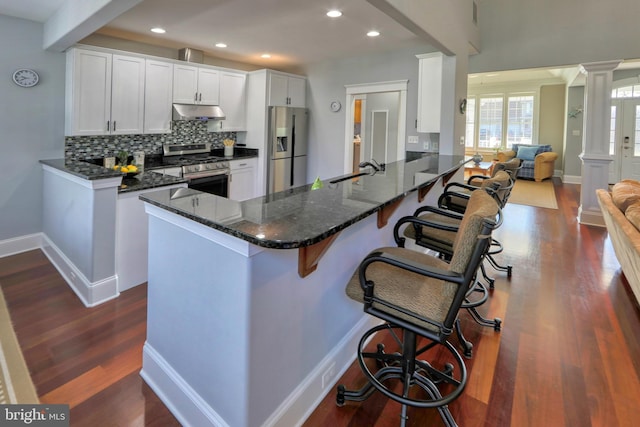 kitchen featuring stainless steel appliances, decorative columns, kitchen peninsula, a breakfast bar area, and white cabinets