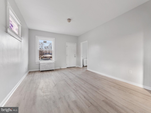 unfurnished room with a wealth of natural light, radiator heating unit, and light hardwood / wood-style floors