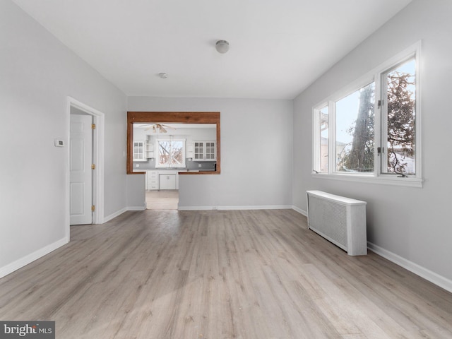 unfurnished living room featuring ceiling fan, radiator heating unit, and light wood-type flooring