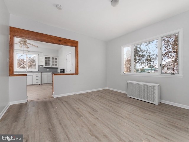 unfurnished living room featuring ceiling fan, light wood-type flooring, sink, and radiator