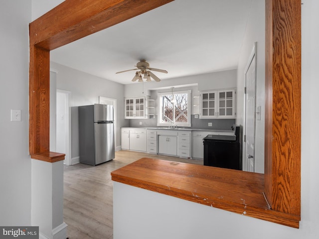 kitchen with stainless steel fridge, white cabinetry, ceiling fan, and sink