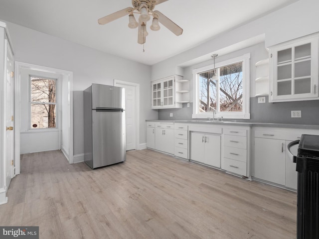 kitchen with electric range oven, white cabinetry, hanging light fixtures, and stainless steel refrigerator