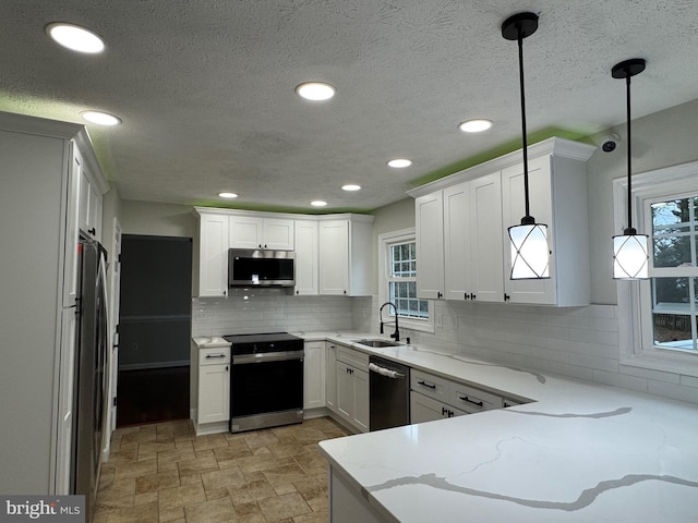 kitchen featuring white cabinets, appliances with stainless steel finishes, hanging light fixtures, and a healthy amount of sunlight