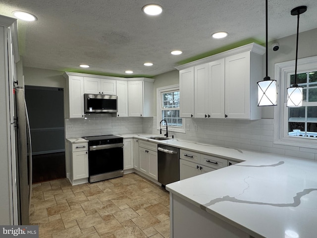 kitchen with sink, hanging light fixtures, backsplash, white cabinets, and appliances with stainless steel finishes