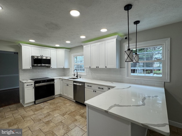 kitchen with white cabinets, sink, hanging light fixtures, light stone countertops, and stainless steel appliances