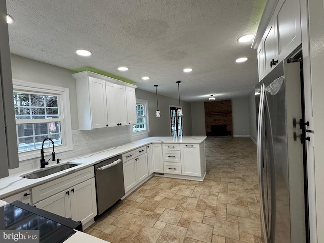 kitchen featuring sink, stainless steel appliances, a brick fireplace, kitchen peninsula, and pendant lighting