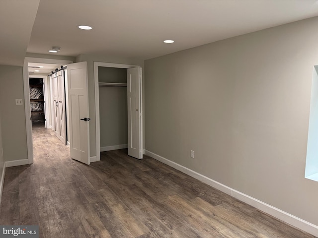 unfurnished bedroom with a barn door, dark hardwood / wood-style flooring, and a closet