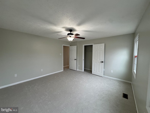 unfurnished bedroom featuring a walk in closet, ceiling fan, carpet floors, and a textured ceiling