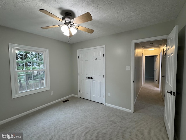 unfurnished bedroom featuring light carpet, a textured ceiling, a closet, and ceiling fan