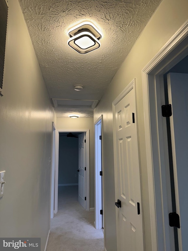 corridor featuring a textured ceiling and light colored carpet